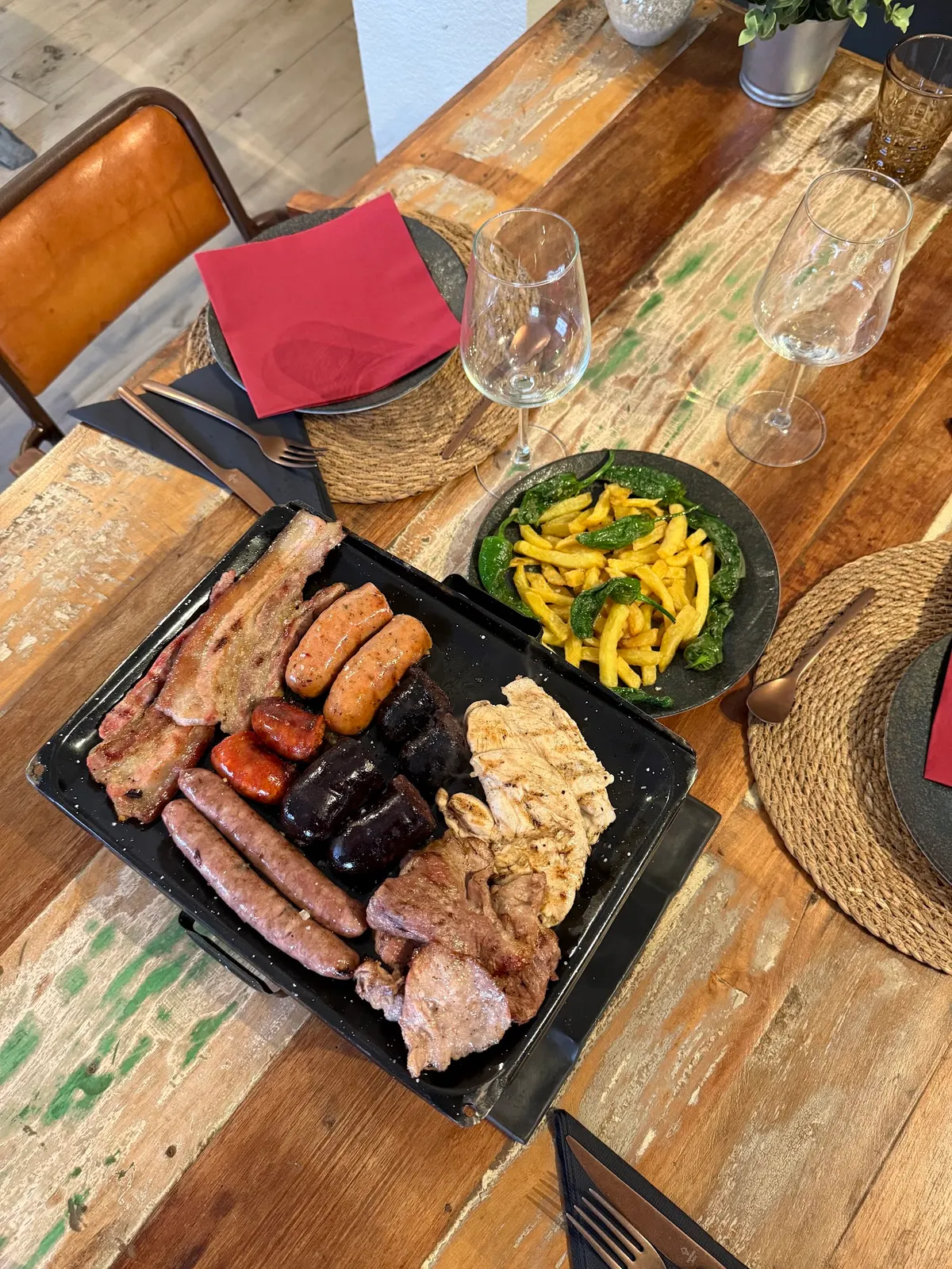Brasero con carnes y embutidos a la brasa en el centro de una mesa de madera